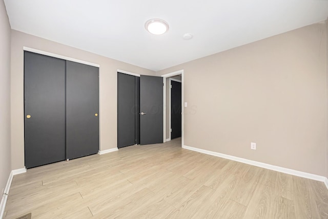 unfurnished bedroom with light hardwood / wood-style flooring and two closets