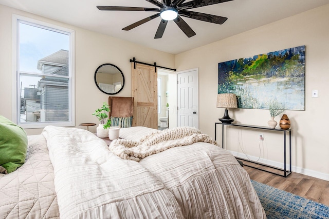 bedroom with light wood-type flooring, ceiling fan, and a barn door