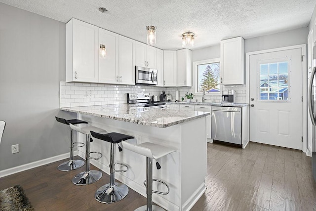 kitchen featuring white cabinetry, backsplash, kitchen peninsula, and appliances with stainless steel finishes