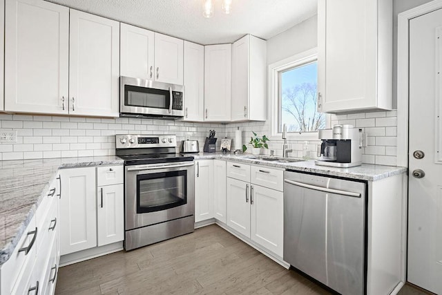 kitchen featuring white cabinetry, appliances with stainless steel finishes, sink, and light stone counters