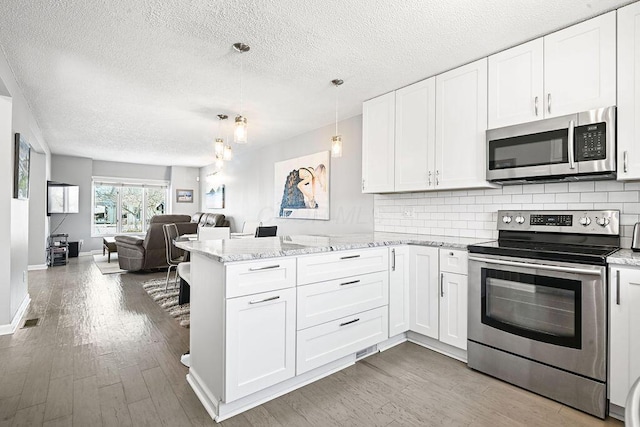 kitchen featuring appliances with stainless steel finishes, pendant lighting, white cabinetry, decorative backsplash, and kitchen peninsula