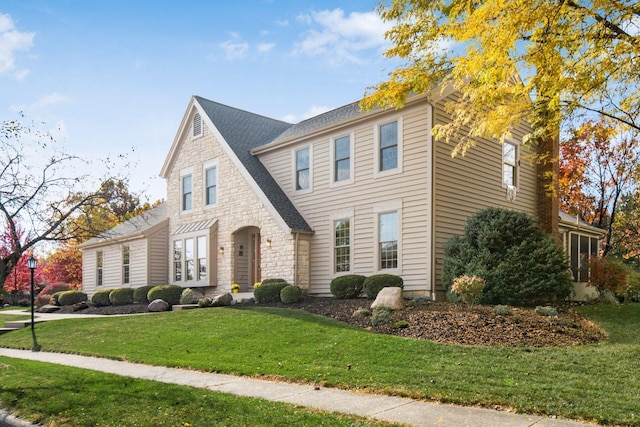 view of front facade with stone siding, a front lawn, and a shingled roof