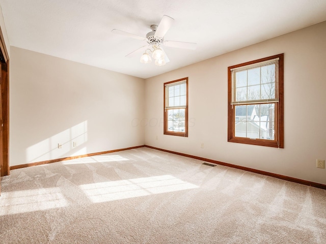 spare room featuring a ceiling fan, light colored carpet, visible vents, and baseboards