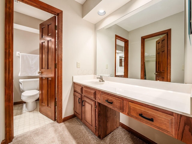 bathroom with toilet, baseboards, a walk in closet, and vanity