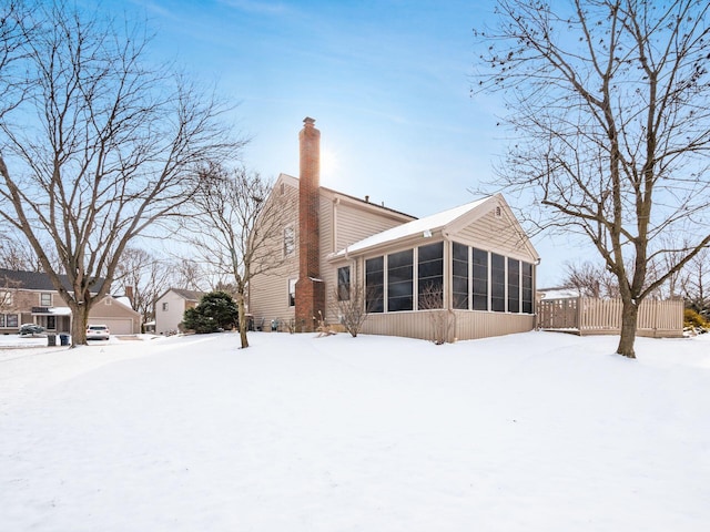 snow covered back of property featuring a sunroom, fence, and a chimney