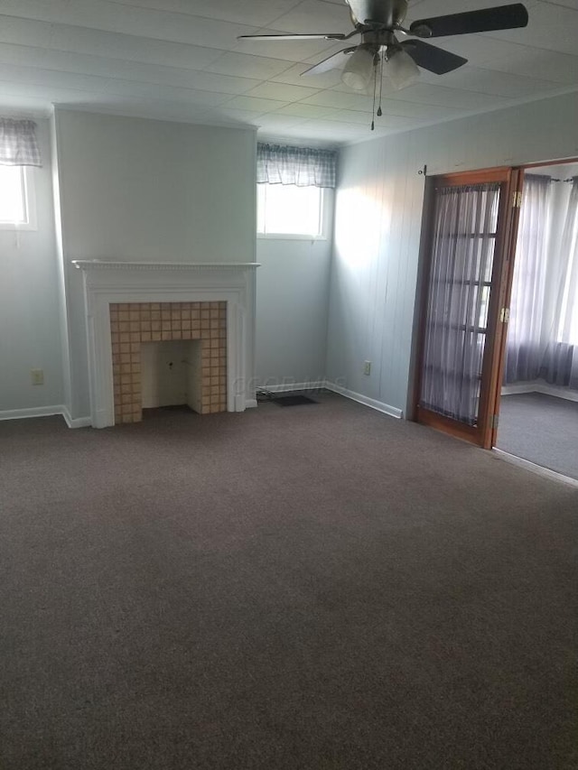 unfurnished living room featuring ceiling fan, carpet flooring, a tiled fireplace, and a healthy amount of sunlight