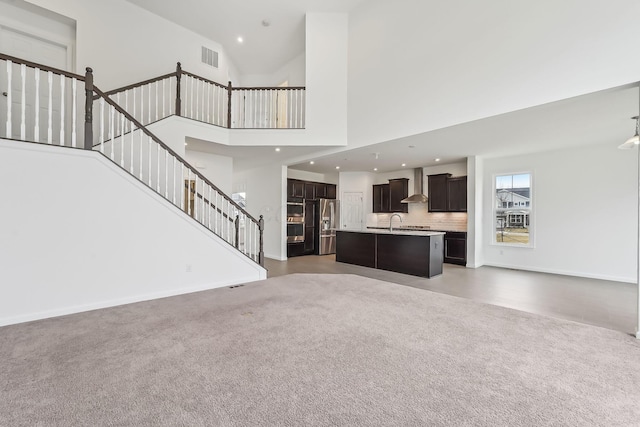 unfurnished living room featuring dark carpet, sink, and a high ceiling