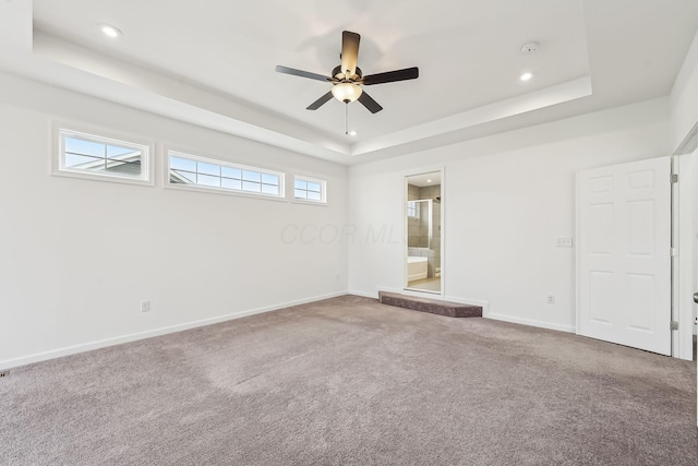 carpeted spare room with a raised ceiling and ceiling fan