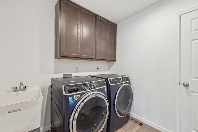 clothes washing area with independent washer and dryer, cabinets, sink, and light wood-type flooring