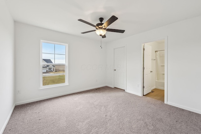 unfurnished bedroom featuring ceiling fan, light colored carpet, and ensuite bath