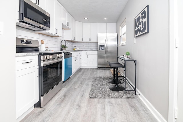 kitchen with appliances with stainless steel finishes, white cabinetry, tasteful backsplash, sink, and light hardwood / wood-style flooring