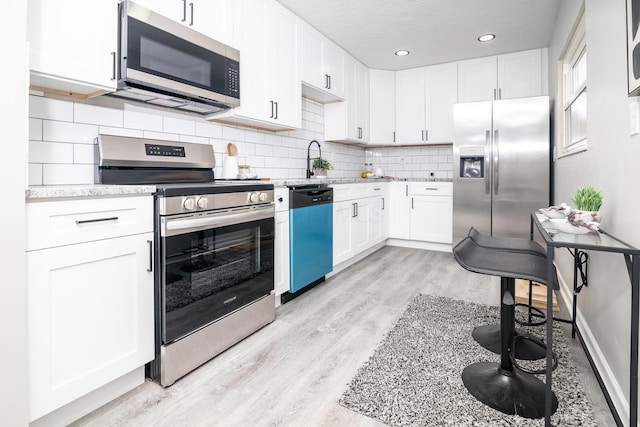 kitchen featuring appliances with stainless steel finishes, sink, white cabinets, tasteful backsplash, and light wood-type flooring