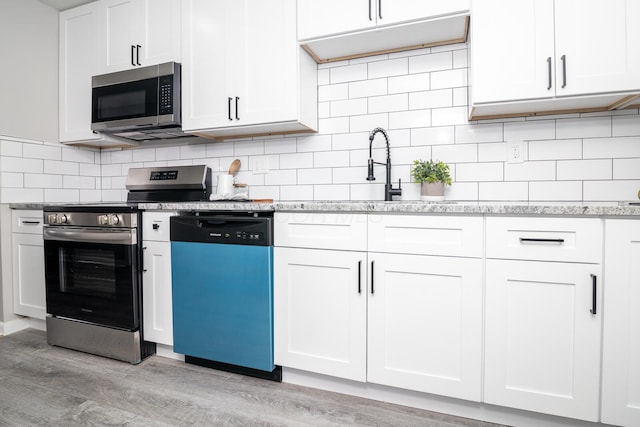 kitchen featuring white cabinets, backsplash, appliances with stainless steel finishes, and light hardwood / wood-style flooring