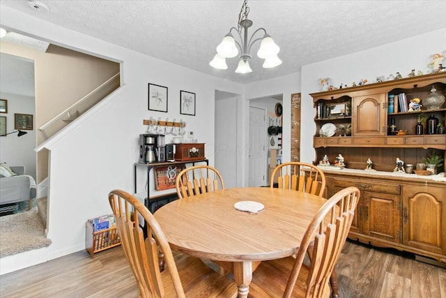 dining area featuring light hardwood / wood-style floors, a textured ceiling, and a notable chandelier