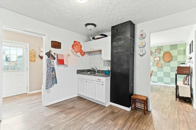 kitchen featuring sink, white cabinetry, a textured ceiling, light hardwood / wood-style floors, and decorative backsplash