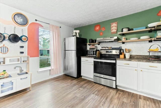 kitchen with appliances with stainless steel finishes, a textured ceiling, decorative backsplash, white cabinets, and light wood-type flooring