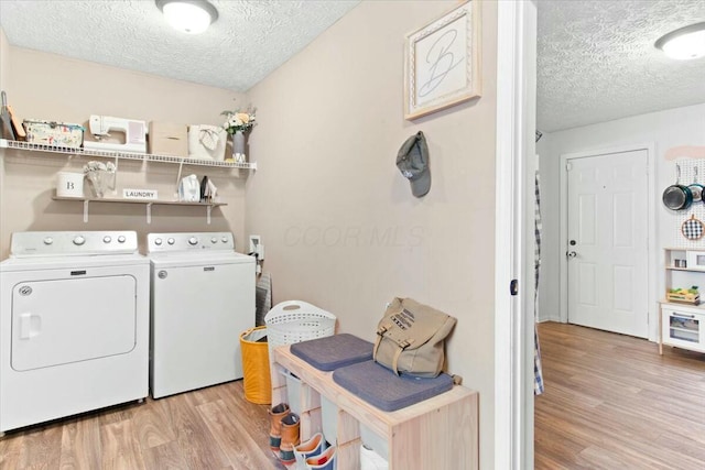 clothes washing area featuring light wood-type flooring, a textured ceiling, and washing machine and dryer