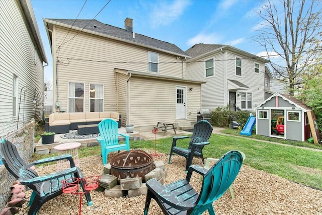 back of property with an outdoor structure, a lawn, and an outdoor living space with a fire pit