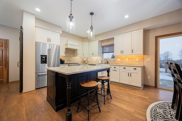 kitchen with high end fridge, white cabinetry, light stone countertops, a kitchen island, and light wood-type flooring