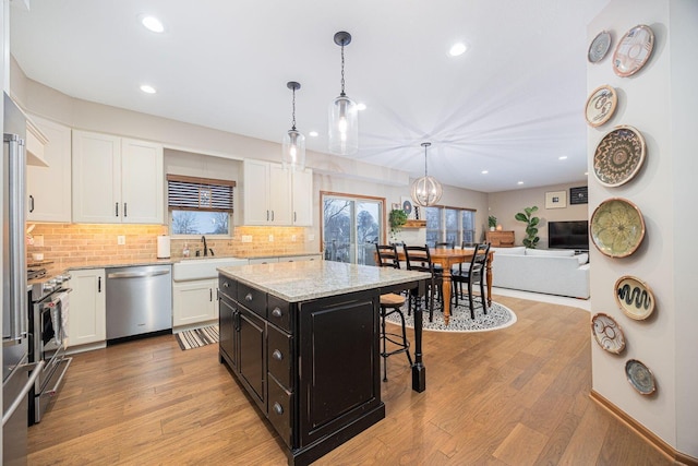 kitchen featuring sink, white cabinetry, a center island, hanging light fixtures, and stainless steel appliances