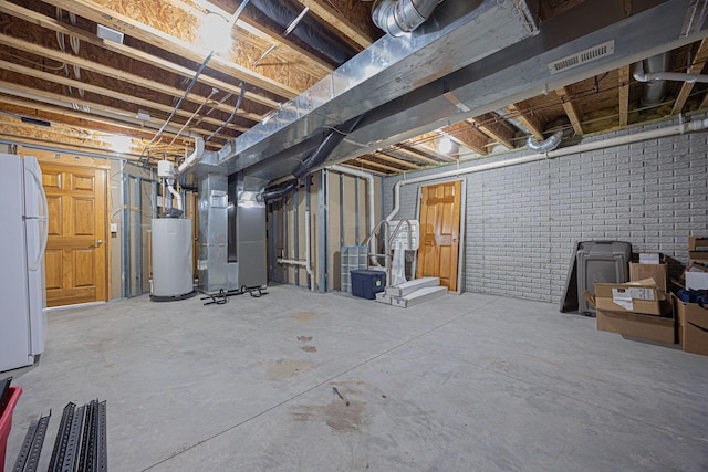 basement featuring heating unit, brick wall, white fridge, and gas water heater