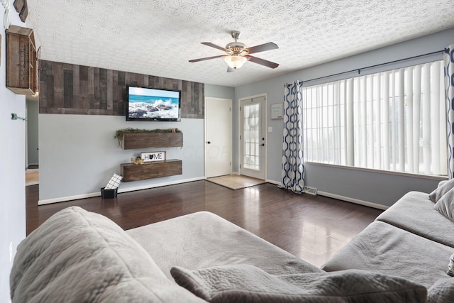 living room featuring dark wood-type flooring, ceiling fan, and a textured ceiling