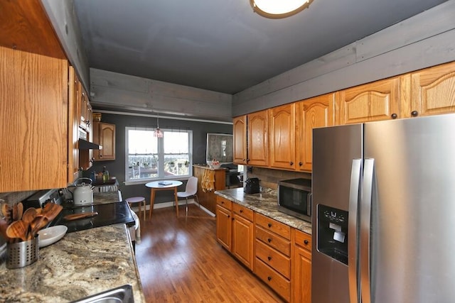 kitchen with wood-type flooring, hanging light fixtures, exhaust hood, light stone counters, and stainless steel appliances