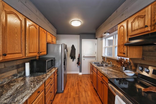 kitchen with stainless steel appliances, sink, light hardwood / wood-style flooring, and dark stone counters