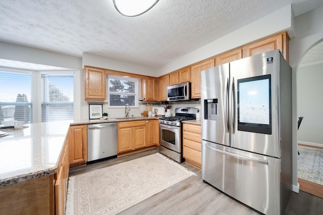 kitchen featuring sink, light hardwood / wood-style floors, stainless steel appliances, light stone countertops, and a textured ceiling