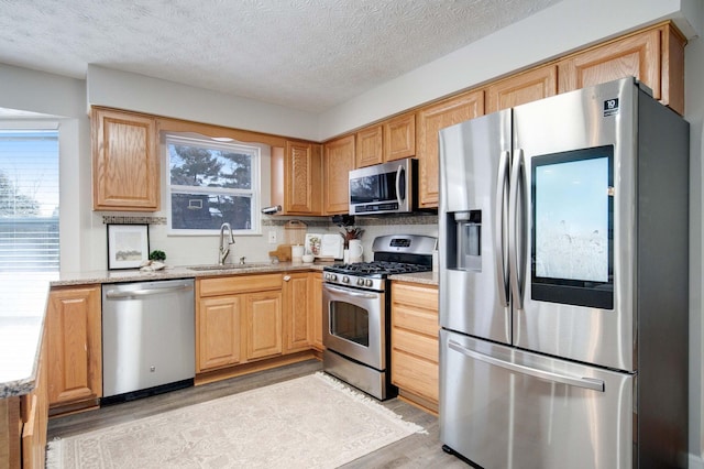 kitchen with sink, light hardwood / wood-style flooring, backsplash, stainless steel appliances, and light stone countertops