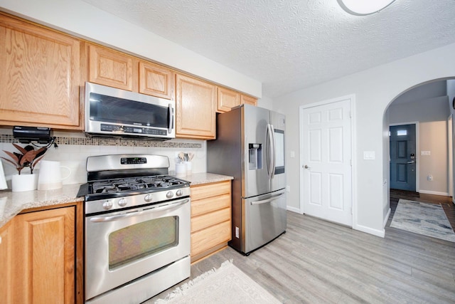 kitchen with appliances with stainless steel finishes, light hardwood / wood-style floors, a textured ceiling, light brown cabinetry, and decorative backsplash