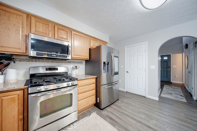 kitchen with light stone counters, stainless steel appliances, a textured ceiling, and backsplash