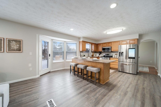 kitchen with hardwood / wood-style flooring, a breakfast bar, a kitchen island with sink, stainless steel appliances, and a textured ceiling