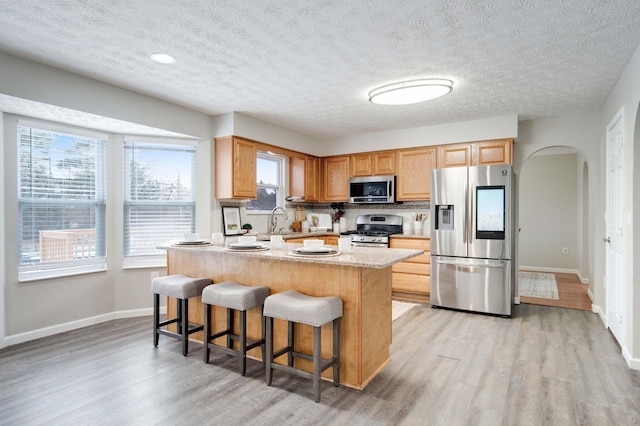 kitchen with appliances with stainless steel finishes, a breakfast bar, light wood-type flooring, a center island, and a textured ceiling