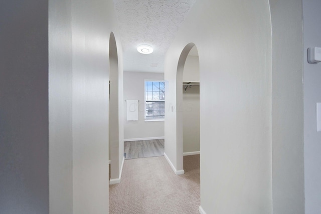 corridor with light colored carpet and a textured ceiling