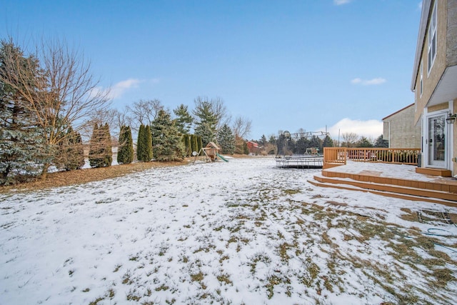 yard covered in snow with a trampoline, a wooden deck, and a playground