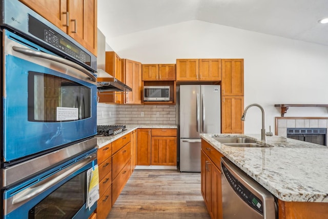 kitchen with appliances with stainless steel finishes, lofted ceiling, sink, decorative backsplash, and light hardwood / wood-style flooring