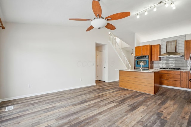 kitchen with black gas cooktop, decorative backsplash, dark wood-type flooring, a center island with sink, and wall chimney exhaust hood