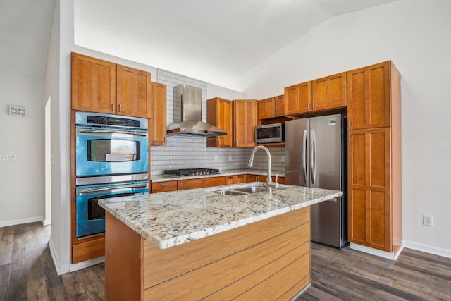 kitchen with sink, vaulted ceiling, an island with sink, stainless steel appliances, and wall chimney range hood