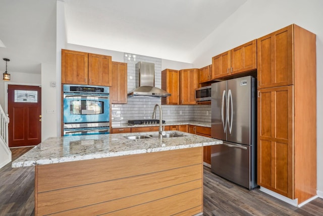 kitchen with tasteful backsplash, an island with sink, stainless steel appliances, light stone countertops, and wall chimney range hood