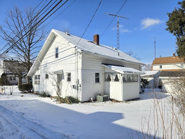 snow covered rear of property featuring central AC