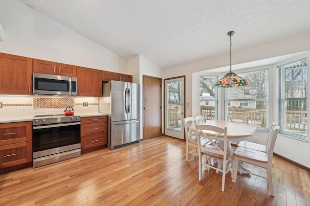 kitchen with decorative light fixtures, light hardwood / wood-style floors, decorative backsplash, and appliances with stainless steel finishes