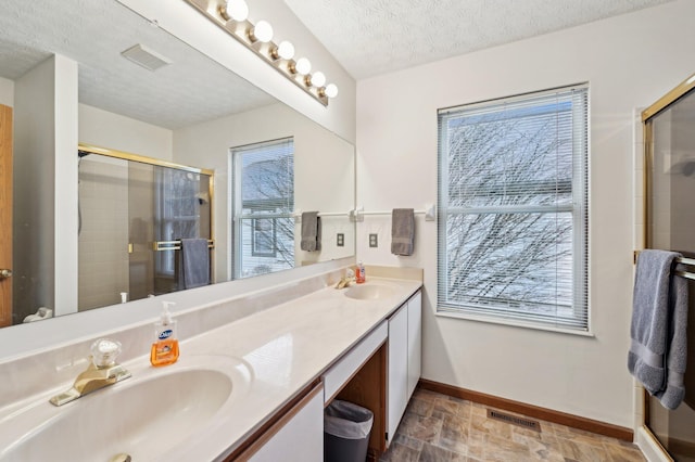 bathroom with vanity, a shower with door, a textured ceiling, and a wealth of natural light