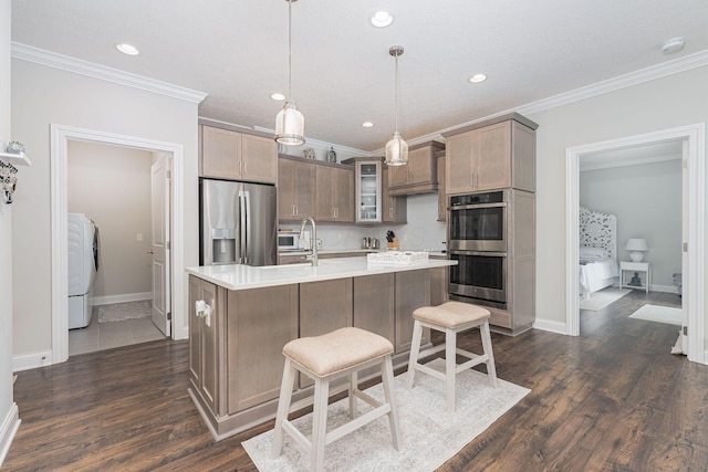 kitchen with crown molding, appliances with stainless steel finishes, a kitchen island with sink, washer / dryer, and decorative light fixtures