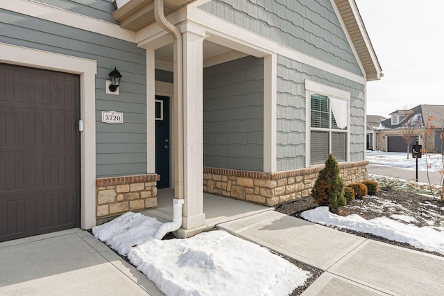 snow covered property entrance featuring a garage and covered porch