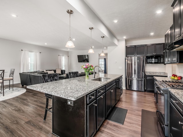 kitchen featuring black appliances, a kitchen island with sink, a kitchen breakfast bar, sink, and dark hardwood / wood-style flooring