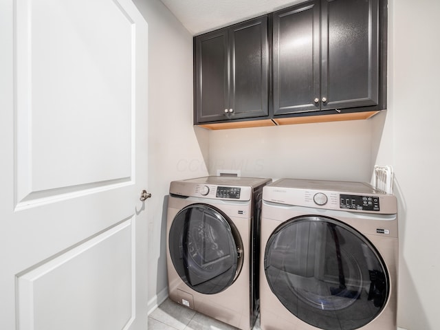 clothes washing area featuring washing machine and clothes dryer, light tile patterned floors, and cabinets