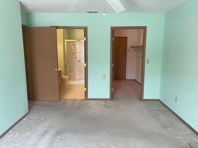 unfurnished bedroom with light colored carpet, a textured ceiling, a walk in closet, connected bathroom, and a closet