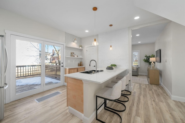 kitchen featuring pendant lighting, sink, a kitchen bar, kitchen peninsula, and light hardwood / wood-style flooring