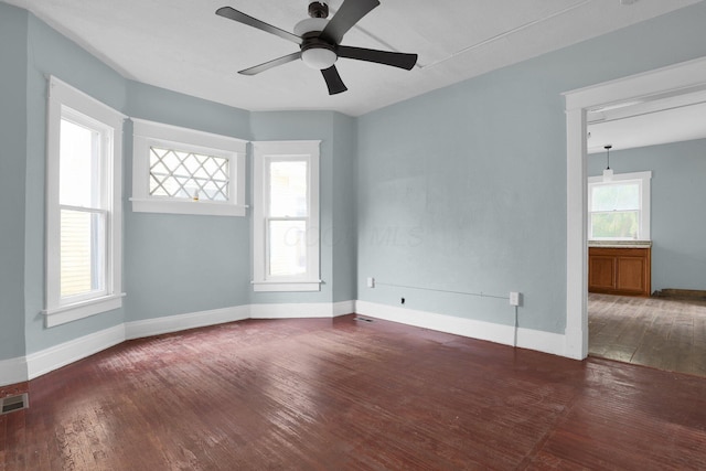 empty room with a healthy amount of sunlight, ceiling fan, and dark hardwood / wood-style flooring